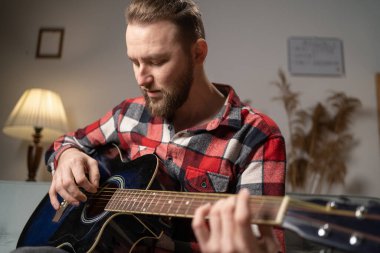 Millennial man playing guitar at home in the evening. Copy space