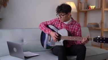 Young man music coach or tutor play guitar have online video lesson on laptop at home. Man artist or singer use musical instrument to record song or single. Hobby concept.