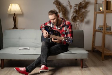 Young man playing guitar at home in the evening. Copy space