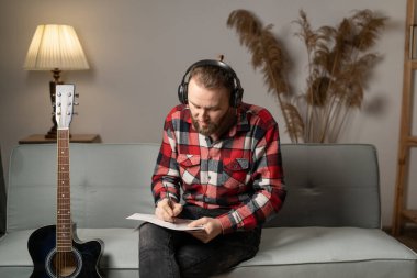 Handsome man with guitar writing lyrics or notes to music book at home studio. people, art, composition concept. Copy space