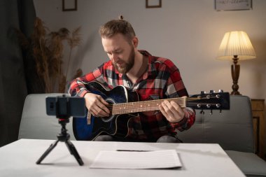 Male blogger teaches guitar playing in an online lesson at home. Copy space