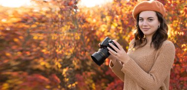 Photographer holding camera outdoors standing in autumn forest on foliage background. Copy space. Banner