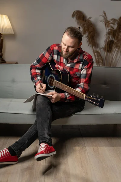 Young caucasian composer man composing song using guitar at home in the evening. Copy space