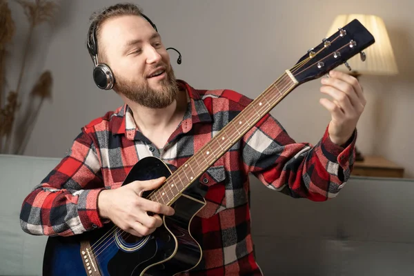 Happy man in headphones with a guitar gives an online lesson to the camera. copy space
