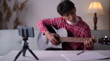 Teenager guy learning to play guitar at home using online lessons. Hobby musical education acoustic guitar. Copy space