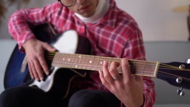 リビングルームのソファに座っている間 若いアラビア人の男性がギターを弾いています 閉じろ — ストック動画