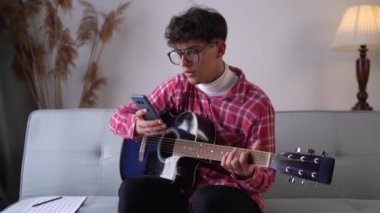 Arabic student playing acoustic guitar while singing a song and record by cellphone for online social. Copy space