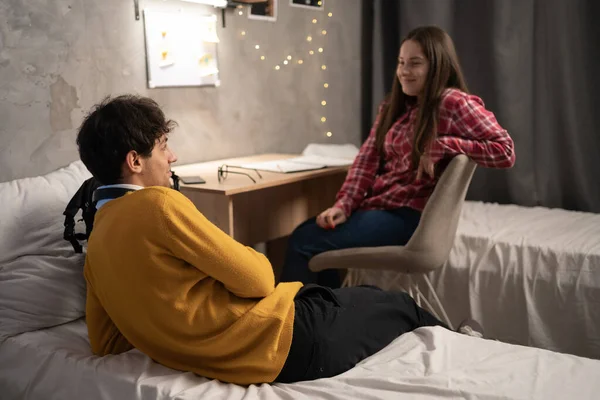 Two casual friends relaxing on beds in dormitory. Young girl and her boyfriend chatting talking about funny things gossip laughing on bed in apartment. Roommates stay in dormitory together. Copy space