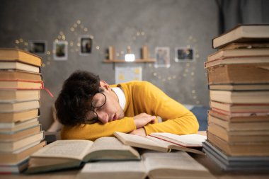 Yurt odasındaki kitapların üzerinde uyuyan gözlüklü yorgun öğrenci. Boşluğu kopyala