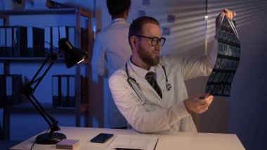 Team focused doctors discussing together history disease of patient using MRI scan during medical meeting at night in hospital. Concept of medicine and health care. Copy space