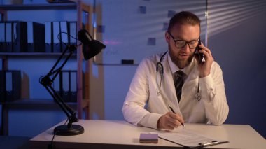 Male doctor in his consulting room, working and phoning. Copy space