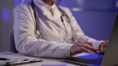 Close up of unknown female doctor sitting at the table in hospital and typing at laptop computer. Copy space