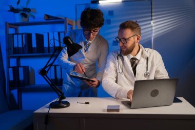 Caucasian male doctor working in hospital using laptop computer speaking and consulting with Arabic male colleague searching analysis or treatment results typing on computer. Copy space