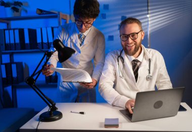 Two doctors colleagues working at hospital office at night shift. Healthcare, medical and technology concept. Copy space