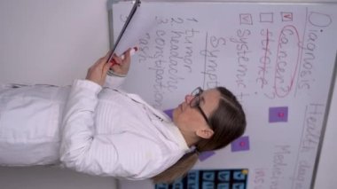 Doctor with stethoscope in white coat holding clipboard, writing medical record diagnosis. Copy space. Vertical video