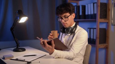 Erkek doktor, gece vardiyası sırasında çalışma masasında kitap okuyor. Boşluğu kopyala