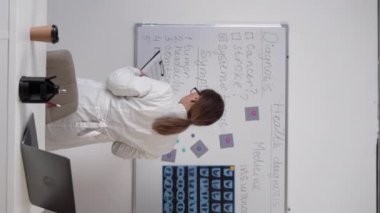 Woman doctor standing with clipboard near blackboard thinking patients diagnosis and symptoms. Copy space. Vertical video
