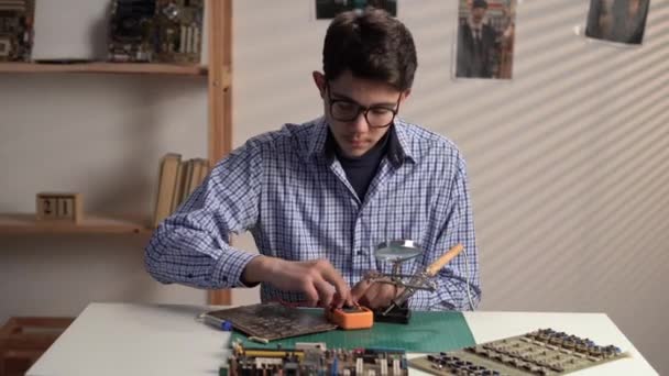 自宅でマルチメーターと学習ロボットを使用してメガネのスマートティーンの男の子 マルチメータによる壊れた回路基板の診断と修正 スペースのコピー — ストック動画