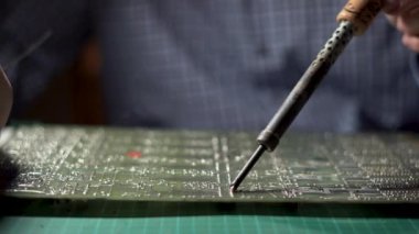Repairman is soldering circuit board of electronic device on the table, close up. He takes tin with a soldering iron and puts it on microcircuit in workshop. Copy space