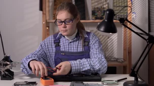 コンピュータの修理とアップグレード ラップトップの修理 若い女性は電子機器用の電圧計を保持します マルチメータを使用してノートパソコンのマザーボードをテストします スペースのコピー — ストック動画