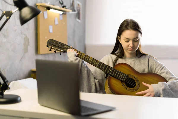 Online training, online classes. Focused asian girl playing guitar and watching online course on laptop while practicing at home. Copy space