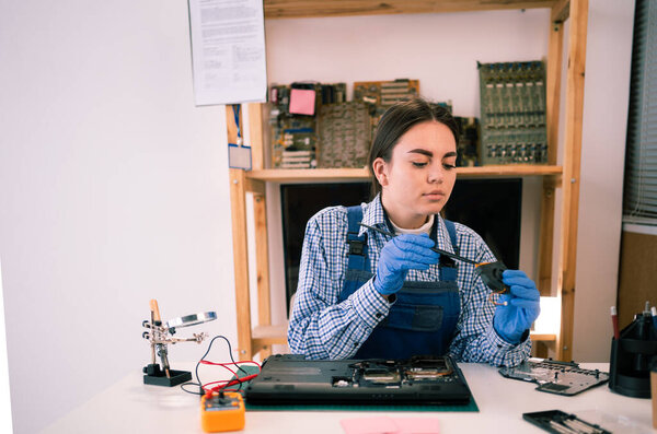 Female repairman working in technical support fixing computer laptop. Disassembling a notebook and cleaning its cooling system. Copy space