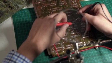 Guy checking circuit board with multimeter on table at home and building a robot as a high school science project, close up. Copy space