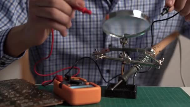 Technik Naprawia Elektronikę Facet Nastolatek Sprawdza Płytkę Drukowaną Multimetrem Stole — Wideo stockowe