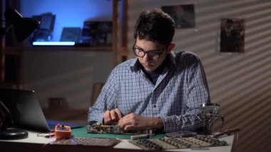 Engineer student inspecting disassembled broken motherboard use laptop with repair video. Technology microelectronics science education concept