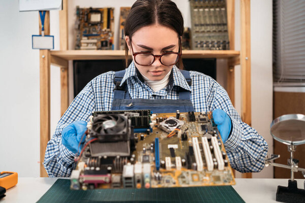 Young repairer disassembling a computer internal parts in service center. Computer female engineer working on an old motherboard. copy space