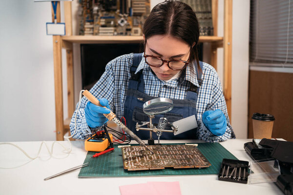 Computer repair engineer soldering circuit board in service center, working on fixing hardware. Copy space