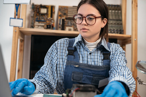 Female computer repairman working on repairing computer in IT workshop watching online courses using laptop. Copy space