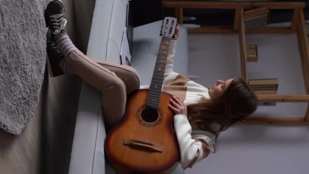 女人在客厅里调音吉他 女士在乐器上弹奏着平静的旋律 放松与歌曲和音乐 创意业余爱好 垂直录像 — 图库视频影像