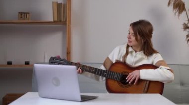 Woman music coach or tutor play guitar have online video lesson on laptop at home studio. Online studying concept. Copy space