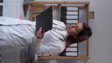 Female doctor talking by mobile phone working in modern clinic, high quality service concept. Vertical video