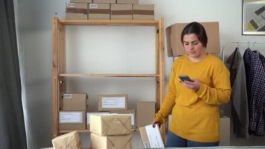 Küçük işletme sahibi bir kadın akıllı telefon kontrol kutusunda mobil uygulama kullanıyor. Çevrimiçi satıcı cep telefonu teknolojisinde perakende satış paketini tarıyor. Posta kutusu barkodu. Boşluğu kopyala