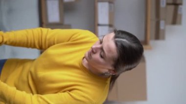 Genç bayan, küçük işletme sahibi. Ofiste çalışıyor. Kıyafetleri kutuda paketliyor. Çevrimiçi pazarlama teslimatı, girişim KOBİ girişimcisi veya serbest kadın konsepti. Dikey video