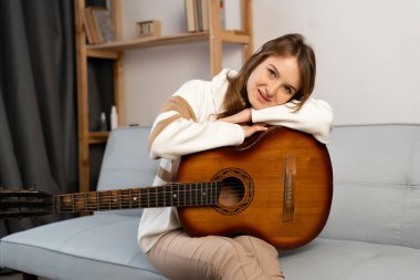 Girl with a guitar on the couch thinking and dreaming about a new song. Copy space
