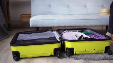 Woman packing suitcase at home, close up. Different clothes packed for journey at home. Travel concept