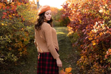 Beautiful girl walking outdoors in autumn collects orange leaves. Young stylish woman enjoying autumn weather. Copy space
