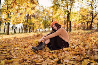 Stylish young woman having rest with leaves in autumn park. Relaxation, enjoying, solitude with nature. Copy space
