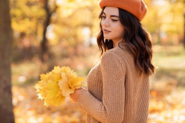 Portrait of a beautiful young woman with autumn leaves in the park. Toned photo with bokeh and copy space.