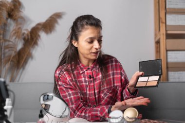 Young woman talking on cosmetics holding a makeup palette while recording her video. Blogger making a video for her blog on cosmetics. Copy space