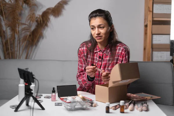 young woman influencer demonstrating cosmetic while talking on camera at home and prepare box for delivery. female beauty blogger broadcast live streaming to review makeup product on social media