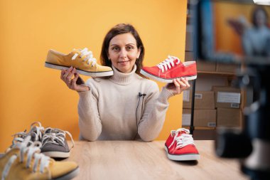 Female blogger or vlogger looking at camera reviewing product, showing shoes. Modern businesswoman using social media for marketing. Copy space