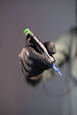 device for tattooing. eyebrow tattooing professional machine. tattoo tool on a gray isolated background is in a hand in black gloves. Copy space
