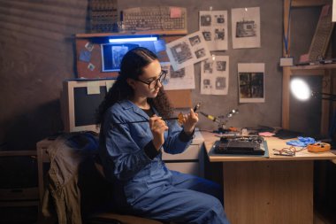 Bilgisayar tamiri, dizüstü bilgisayarı küçük fırçayla temizleyen genç bir kadın, soğutma, dizüstü bilgisayarın sıcaklığı, fan, toz kirliliği. Eski retro tamir atölyesinde dizüstü bilgisayar servisi. Boşluğu kopyala