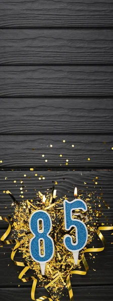 暗い木製の背景に数字85青お祝いのろうそくと金のコンフェッティ 85歳の誕生日カード 記念日と誕生日のコンセプト 縦のバナー スペースのコピー — ストック写真