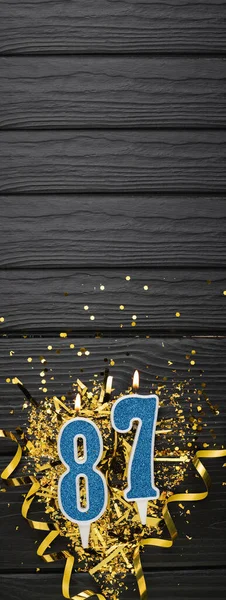 暗い木製の背景に87青のお祝いのろうそくと金のコンフェッティ 87歳の誕生日カード 記念日と誕生日のコンセプト 縦のバナー スペースのコピー — ストック写真