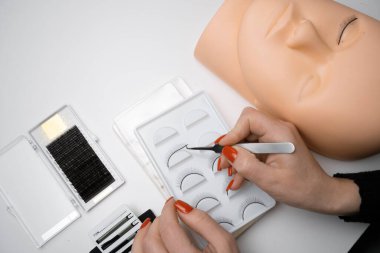 Silikon manken ve cımbızda kirpikleri var. Kirpik eklentilerini çalıştırıyorum. Göz bağı, oyuncak bebek modelinin yüzünü ustaca dizer. Boşluğu kopyala